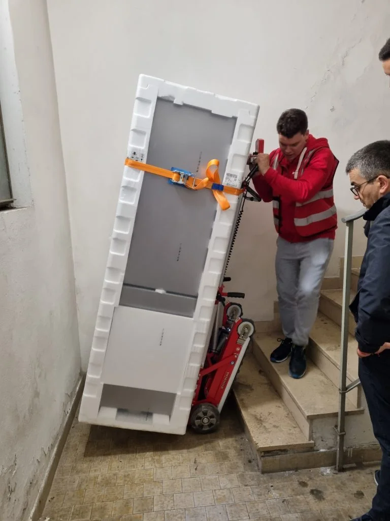 Un hombre transporta un electrodoméstico por las escaleras con la carretilla eléctrica sube escaleras  Buddy Lift.